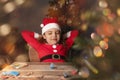 6 yearold girl in Santa Claus costume dreaming with closed eyes at table with decor for Christmas tree Royalty Free Stock Photo