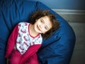 6 years girl child in pink pajamas lay on blue ottoman and looks up with smile. day of sleep. Happiness, leisure and lifestyle in