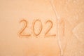 Years 2021 are inscribed on sandy beach on yellow sand close-up. The sea wave washes away the inscription 2021. The concept of