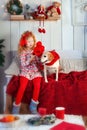 5 years old blonde girl in red outfit dress her golden dog in red scarf and hat. Child and dog seat on red sofa in cozy living Royalty Free Stock Photo