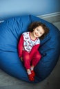 6 years old blue eyed girl child in pink pajamas and red socks lay on blue ottoman and looks up with smile. day of sleep.