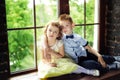 6 years old boy in blue bow tie and white shir hugging little 5 years old curly girl in yellow dress. Children sitting on window. Royalty Free Stock Photo