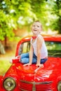 5 years old boy in blue jeans, white t-shirt and red bow tie sit on red retromobile old car and look up. Happy child outdoor.