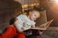 3-4 years old boy is reading a book sitting on a sofa with teddy bear. Home reading of fairy tales. Cute little boy is Royalty Free Stock Photo