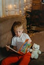 3-4 years old boy is reading a book sitting on a sofa with teddy bear. Home reading of fairy tales. Cute little boy is Royalty Free Stock Photo