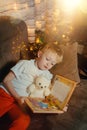 3-4 years old boy is reading a book sitting on a sofa with teddy bear. Home reading of fairy tales. Cute little boy is Royalty Free Stock Photo