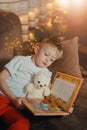 3-4 years old boy is reading a book sitting on a sofa with teddy bear. Home reading of fairy tales. Cute little boy is Royalty Free Stock Photo