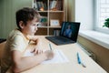 8 years old boy sit by desk with laptop and do writing task during online lesson Royalty Free Stock Photo