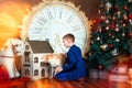 6 years old boy sit on floor, look in dollhouse with dog. Rocking horse and big clock near. New year eves, christmas tree and Royalty Free Stock Photo