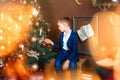 6 years old boy sit and look at beautiful christmas tree. Christmas lights around. Christmas eves and gifts. Child wait for Royalty Free Stock Photo