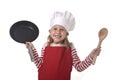 6 or 7 years old little girl in cooking hat and red apron playing cook smiling happy holding pan and spoon Royalty Free Stock Photo