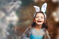 6 years old smiling girl with rabbit ears on head in blooming trees in spring. Child pretends to be easter bunny. Happy Easter