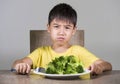 7 or 8 years old upset and disgusted hispanic kid sitting on table in front of broccoli plate looking unhappy rejecting the fresh