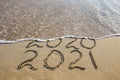 2020, 2021 years written on sandy beach sea. Wave washes away 2020 Royalty Free Stock Photo