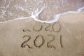 2020, 2021 years written on sandy beach sea. Wave washes away 2020 Royalty Free Stock Photo