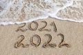 2021, 2022 years written on sandy beach sea. Wave washes away 2021