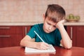 7 yeas old boy sitting at table in the kitchen and writing notes on sheets