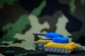 Yellow-blue tanks figures on camouflage background, Ukrainian flag colors on toy tank figures, anti-war concept Royalty Free Stock Photo