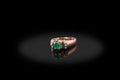 Yello gold precious ring female with diamonds and big emerald on black background.