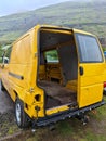 A yellow abandoned transporter car with a missing door in the back