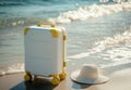 Yellow-accented suitcase and straw hat on sandy beach at ocean edge Royalty Free Stock Photo