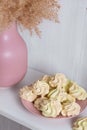 Yellow airy meringue on pink plate near a vase with reeds on a white background