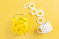 Yellow alarm clock with daisies instead of a dial and a white mug. Royalty Free Stock Photo