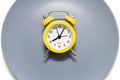 A yellow alarm clock lies on a plate on a white background Royalty Free Stock Photo