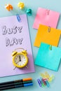 Yellow alarm clock on a purple card with the inscription `busy day` colored office staples, cards, pens, crumpled balls of paper. Royalty Free Stock Photo