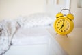 Yellow alarm clock standing on nightstand in background of bed in interior of room. bed`s not made.