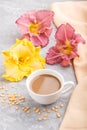 Yellow anf purple day-lilies cup of coffee on a gray concrete background, with orange textile. Side view, close up Royalty Free Stock Photo