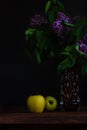 Yellow apples and purple lilac with fresh green leaves in a vase on black wooden background still life. Spring flowers Royalty Free Stock Photo