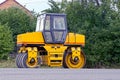 Yellow asphalt paver standing by the roadside near trees