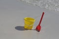 A yellow baby bucket and a red shovel stand on the sand by the sea Royalty Free Stock Photo