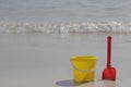 A yellow baby bucket and a red shovel stand on the sand by the sea Royalty Free Stock Photo