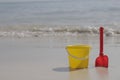 A yellow baby bucket and a red shovel stand on the sand by the sea Royalty Free Stock Photo