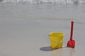 A yellow baby bucket and a red shovel stand on the sand by the sea Royalty Free Stock Photo