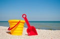 Yellow baby bucket with red toy toy red plastic spatula on the left against the blue sea sea sand summer sunny day, baby toys Royalty Free Stock Photo