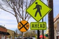 A yellow and back pedestrian walking sign with a yellow and black railroad crossing sign with blue sky and buildings Royalty Free Stock Photo