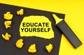 On a yellow background, a black sheet on which lies yellow paper with the inscription - Educate Yourself Royalty Free Stock Photo