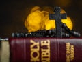 On a yellow background with flickering lights lies a book - the Holy Bible, on it is a rosary with a Catholic cross. Macro shot. Royalty Free Stock Photo