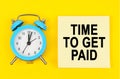 On a yellow background lie a clock and a sticker sheet with the inscription - TIME TO GET PAID Royalty Free Stock Photo