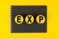 On a yellow background lies a black notebook, yellow wooden circles with the inscription - EXP