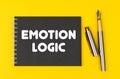 On a yellow background lies a pen and a black notebook with the inscription -Emotion Logic