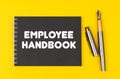 On a yellow background lies a pen and a black notebook with the inscription - Employee Handbook Royalty Free Stock Photo