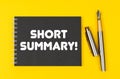 On a yellow background lies a pen and a black notebook with the inscription - Short Summary