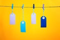 On a yellow background photographed labels. Four colorful empty labels hang on a rope pinned with clothespins. Bright