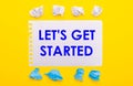 On a yellow background, white and blue crumpled pieces of paper and a notebook with the text LET IS GET STARTED Royalty Free Stock Photo