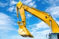 Yellow backhoe with hydraulic piston arm against blue sky. Heavy machine for excavation in construction site. Hydraulic machinery.