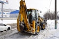 Yellow backhoe loader JCB-3CX clears the snow. Cloudy winter view.